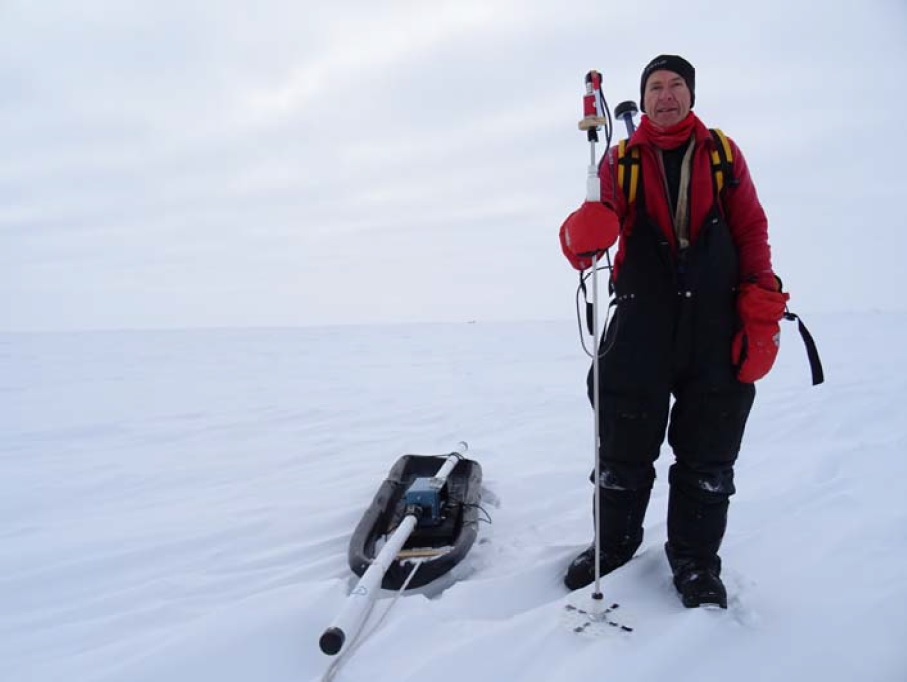 Supplementary Figure 1 from Haas et. al (2017) Original caption: Photo of the EM31SH ice thickness sounder and Magnaprobe snow thickness sensor used in this study. The EM instrument is strapped onto a toboggan dragged by one person and operated in horizontal dipole mode. The Magnaprobe is carried by another person. Note rather level ice surface morphology (Site 5; cf. Figure 2) and Twin Otter aircraft in the background (small black spot).